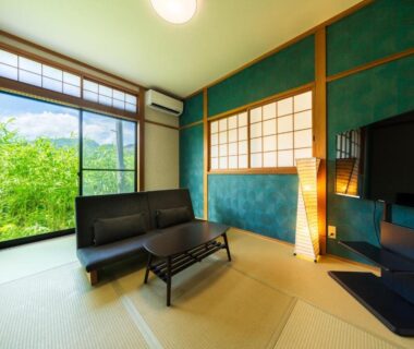 Tatami room with low sofa, shoji screens and large window overlooking green hillside at Yufuin Hanarenoyado Yukagetsu in Oita