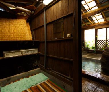 Indoor wooden bath area with stone tub and lattice screens at Yufuin Inakamura Inakaso Ōita Kyūshū Japan