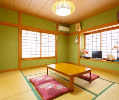 Tatami room with low table, floor cushions, shoji screens and television on windowsill at Yufuin Inakamura Inakaso Oita