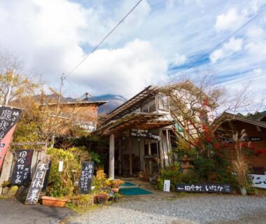 Front entrance of Yufuin Inakamura Inakaso with wooden porch, vertical banners and potted plants on gravel courtyard, Ōita