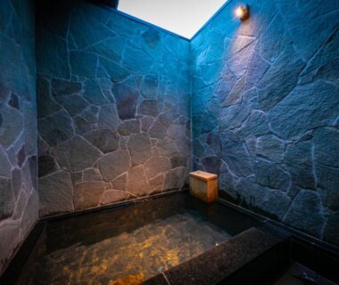 Enclosed stone-walled onsen bath with skylight and wooden stool at Yufuin Kaze no Mori, Ōita
