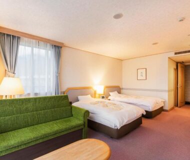 Bright twin room with two beds, green sofa, low wooden table and window at Yufuin Kotobuki Hananosho in Oita