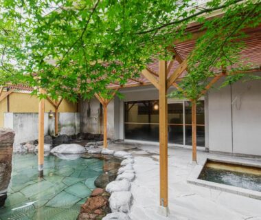 Outdoor stone onsen courtyard with wooden pergola and small soaking tub at Yufuin Kotobuki Hananosho, Ōita