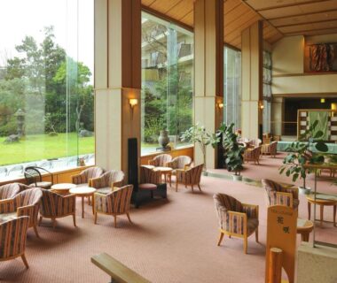 High-ceiling lounge with floor-to-ceiling windows and seating at Yufuin Kotobuki Hananosho in Ōita, Kyūshū