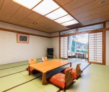 Traditional tatami room with low table, floor cushions, shoji screens and balcony view toward green hills