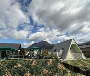 Triangular A-frame building and low cottages with mountain backdrop at Yufuin Onsen 8A1 Yaeichi Oita