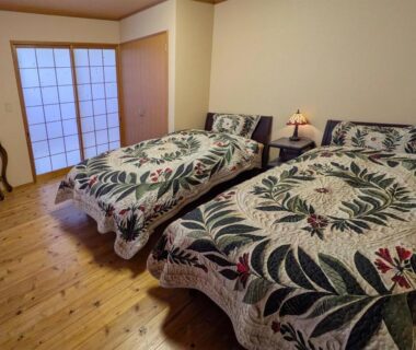 Twin Western beds with patterned quilts, wooden floor, shoji sliding door and bedside lamp in Yufuin ryokan room