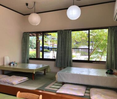 Tatami room with low tables, floor cushions and green garden view at Yufuin Onsen Hasuwa Inn, Ōita