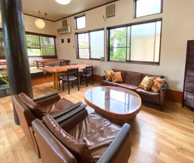 Communal lounge with tatami seating, leather sofas, wooden floor and large windows at Yufuin Onsen Hasuwa Inn, Ōita