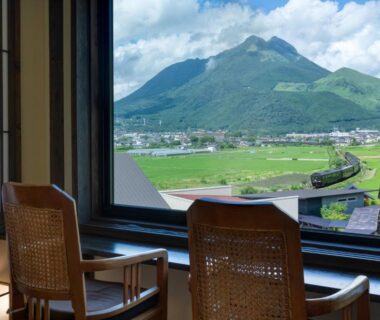 Two woven chairs by window with mountain and green field view at Yufuin Onsen Toshoan, Ōita, Kyūshū