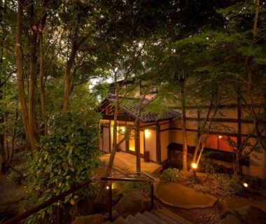 Warm-lit wooden entrance pathway through trees at Yufuin Onsen Toshoan in Ōita, Kyūshū, Japan
