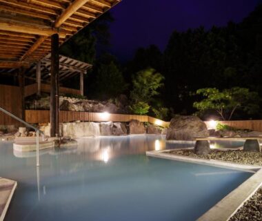 Nighttime outdoor onsen with wooden shelter, stone edging and surrounding garden at Yufuin Onsen Tsukanoma Oita