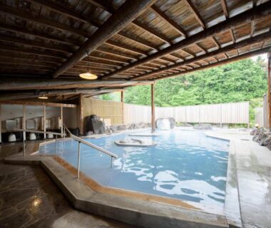 Covered communal onsen with wooden roof, bathing steps and washing stations at Yufuin Onsen Tsukanoma, Ōita