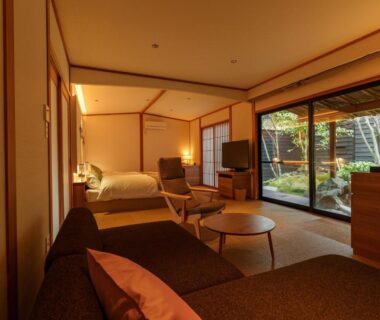 Tatami room with bed, sofa and sliding glass doors opening to a courtyard at Yufuin Rakuyu in Ōita, Kyūshū, Japan