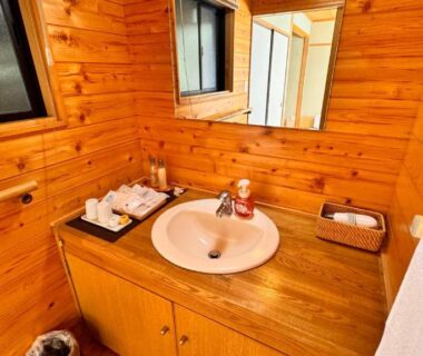 Compact wooden washbasin and mirror inside Yufuin Ryokan Yamanami bathroom, Ōita, Kyūshū