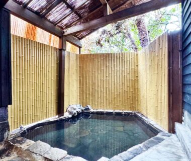 Stone-edged onsen bath with bamboo fence and wooden roof at Yufuin Ryokan Yufumomiji, Ōita