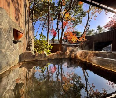 Stone and wooden onsen bath with autumn foliage reflections at Yufuin Ryokan Yufumomiji, Ōita