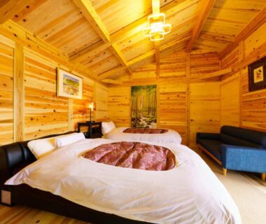 Twin beds in wood-paneled ryokan room with vaulted ceiling and small sofa at Yufuin-Sanso Waremokou Oita