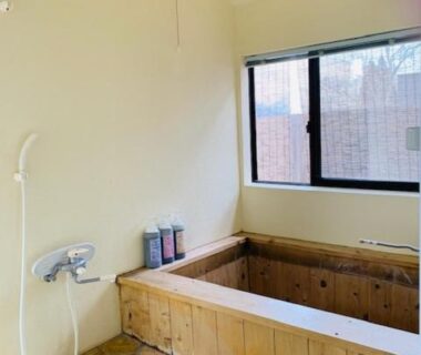 Wooden soaking tub with handheld shower, stone floor and window in a ryokan room in Ōita