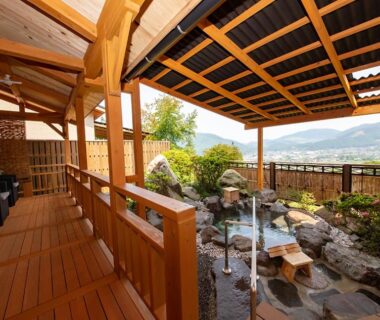 Covered wooden terrace with stone outdoor onsen bath and mountain view at Yufuin-Sanso Waremokou, Ōita