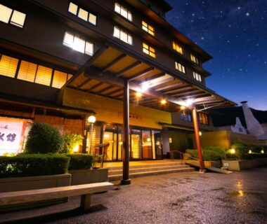 Nighttime exterior of Yufuin Sansuikan with lit entrance canopy, warm windows and wet courtyard paving