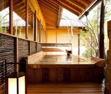 Wooden soaking tub on covered terrace with bamboo screens and lanterns at Yufuin Santoukan, Ōita