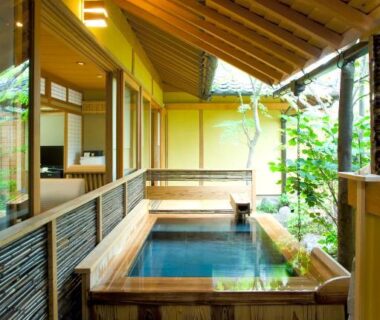Covered wooden onsen bath on veranda with sliding shoji, adjoining room and small garden view in Ōita