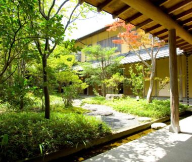 Serene ryokan courtyard with wooden covered walkway and stone path surrounded by lush garden at Yufuin Santoukan Ōita