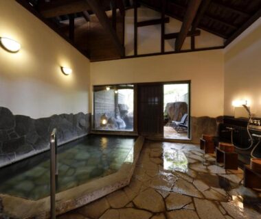 Stone-lined indoor onsen with wooden ceiling, wash stations and stone floor at Yufuin Souan Kosumosu, Oita