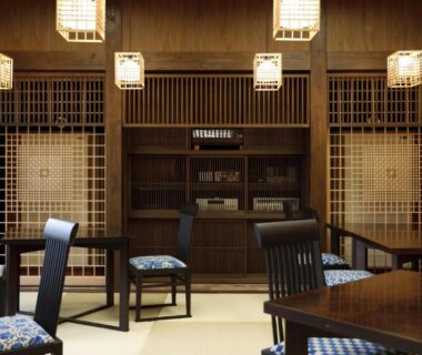 Interior dining room with tatami flooring, wooden lattice screens, hanging lanterns and cushioned chairs at a ryokan in Ōita Kyushu