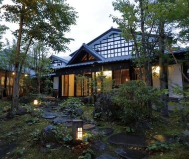Traditional ryokan building framed by moss garden and lanterns at dusk in Yufuin, Oita