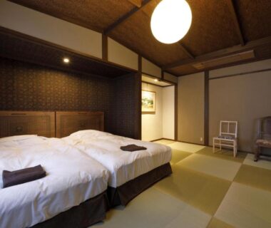Tatami-floored twin room with low beds, shoji screens and warm wooden ceiling at Yufuin Souan Kosumosu in Oita