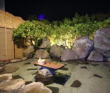 Night-lit outdoor stone bath with low wooden table and rock enclosure at Yufuin Tabinokura, Ōita