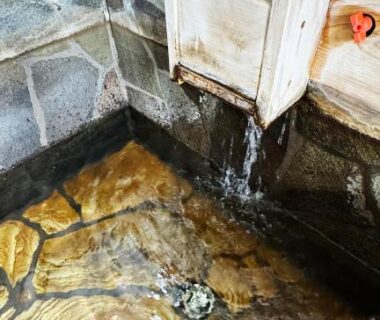 Indoor stone onsen bath with wooden spout and three rubber ducks at Yufuin Tabinokura, Ōita