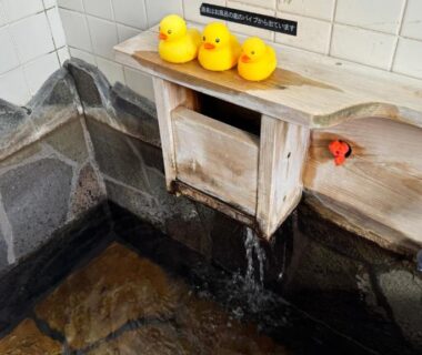 Wooden spout filling stone onsen bath with rubber ducks at Yufuin Tabinokura in Ōita