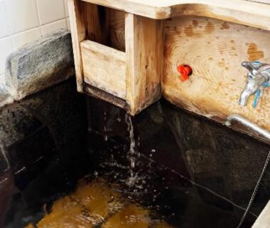 Wooden spout filling small stone bath basin at Yufuin Tabinokura, Oita