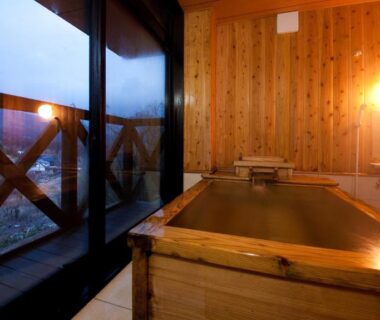 Warm-lit interior with wooden soaking tub and large window overlooking distant town