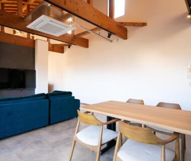 Open-plan living with blue sofa, wooden dining table and exposed ceiling beams at Yufuin Tsubaki in Ōita