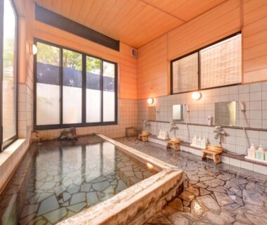 Indoor stone onsen bath with wooden ceiling and washing stations at Yufuin Yamaboushi, Ōita, Kyūshū