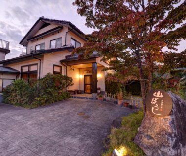 Traditional two-story ryokan entrance with lit stone marker at Yufuin Yamaboushi in Oita, maple tree