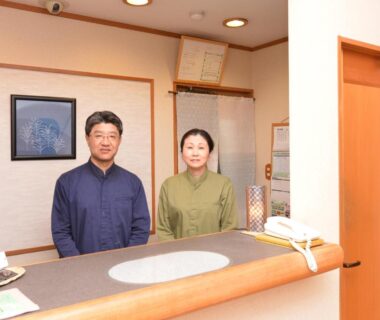 Ryokan hosts standing behind wooden reception counter at Yufuin Yamaboushi in Ōita, Kyūshū
