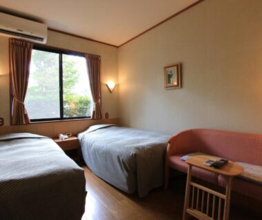 Twin bedroom with two single beds, sofa and window overlooking greenery at Yufuin Yamaboushi, Oita