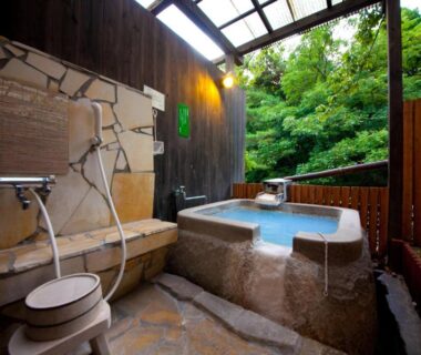 Stone bathing tub with wooden shower area in open-air onsen setting at Yufuin Yasuha, Ōita, Kyūshū, Japan