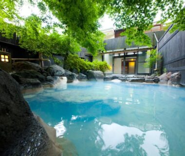 Milky blue outdoor onsen pool with rocks and trees at Yufuin Yasuha in Ōita