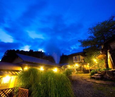 Lit ryokan buildings and stone path under deep blue evening sky at Yufuin Yasuha, Ōita