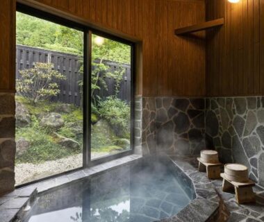 Indoor stone onsen bath with wooden walls and garden view at Yufusaryo in Ōita, Kyushu