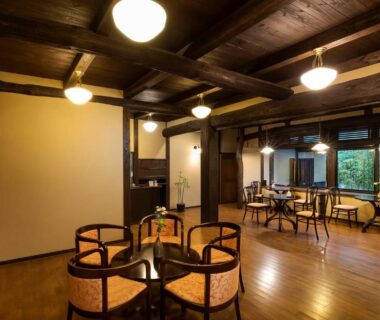 Spacious wooden-beamed lounge with chairs and garden-facing windows at Yufuin Yufusaryo, Ōita