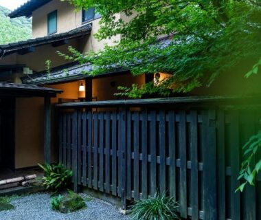 Gravel courtyard and wooden fence at Yufuin Yufusaryo in Ōita, framed by lush green trees