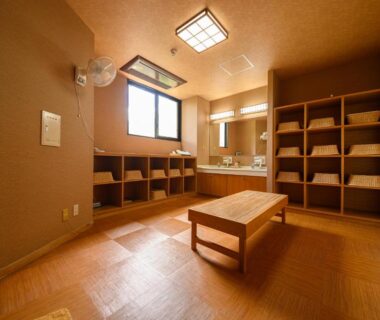 Communal changing area with wooden bench, cubby shelves, washbasins and mirrors at YufuinOnsenRyokan in Ōita