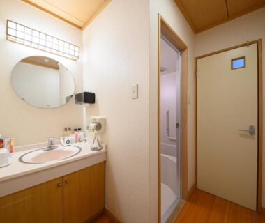 Vanity with round mirror and sink, doorway to bathing area in YufuinOnsenRyokan Mebaeso, Ōita